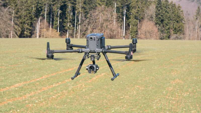 A DJI Matrice M300 drone in flight over a grassy field.