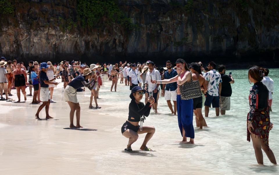 Tourists gather along the beach and take photos at Maya Bay on the Thai island of Phi Phi Leh