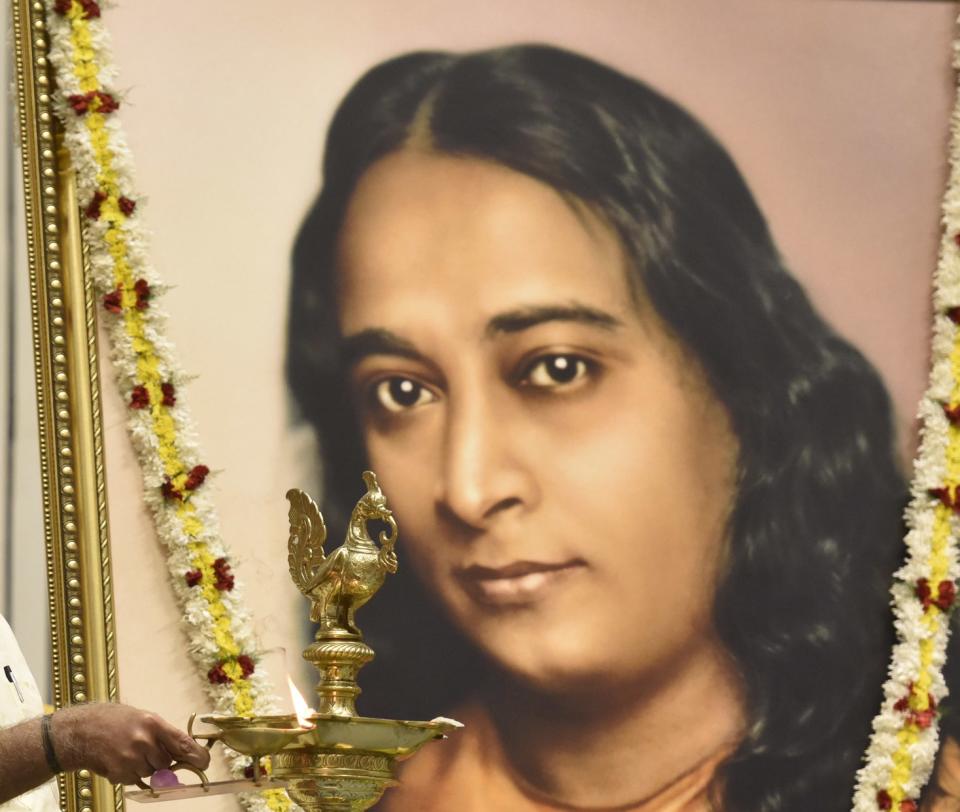 A man lights a lamp in front of a portrait of Paramahansa Yogananda