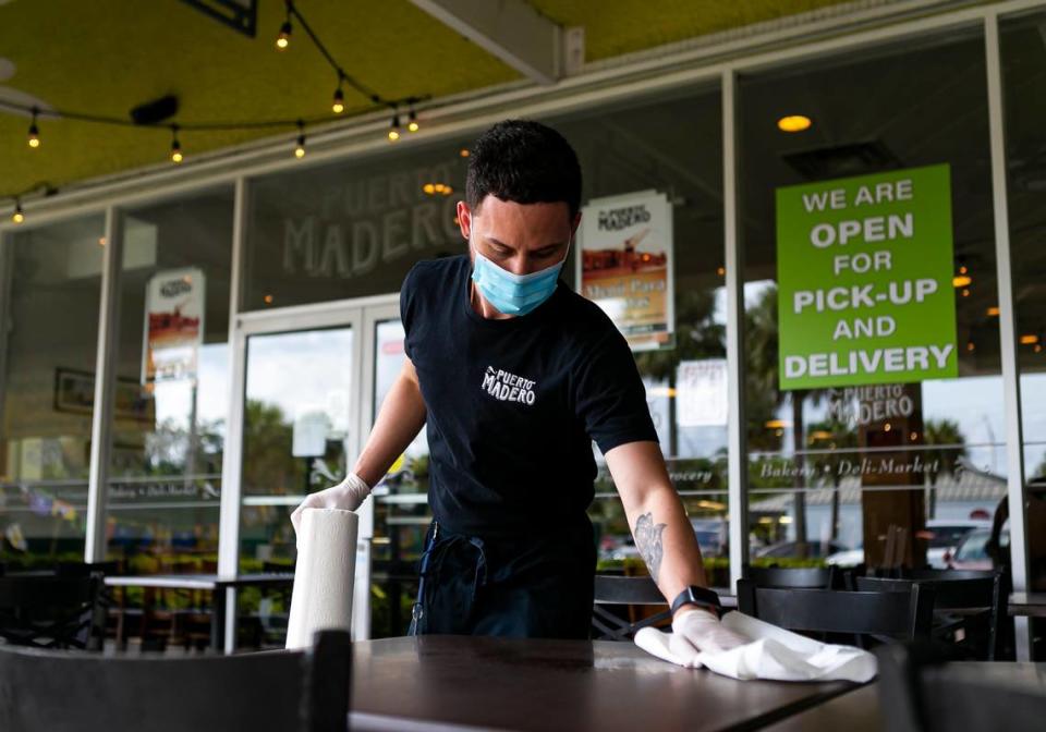 Juan Pablo Tarrago, 26, a waiter, cleans tables outside of Puerto Madero in Kendall on the first day Miami-Dade County allowed restaurants to reopen their dining rooms on Monday, May 18, 2020. 
