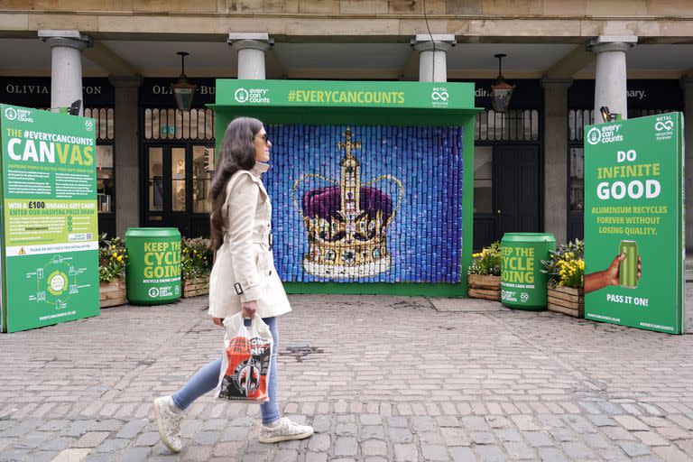 Una mujer pasa frente a la instalación de una corona hecha con latas recicladas, en Covent Garden Market, Londres