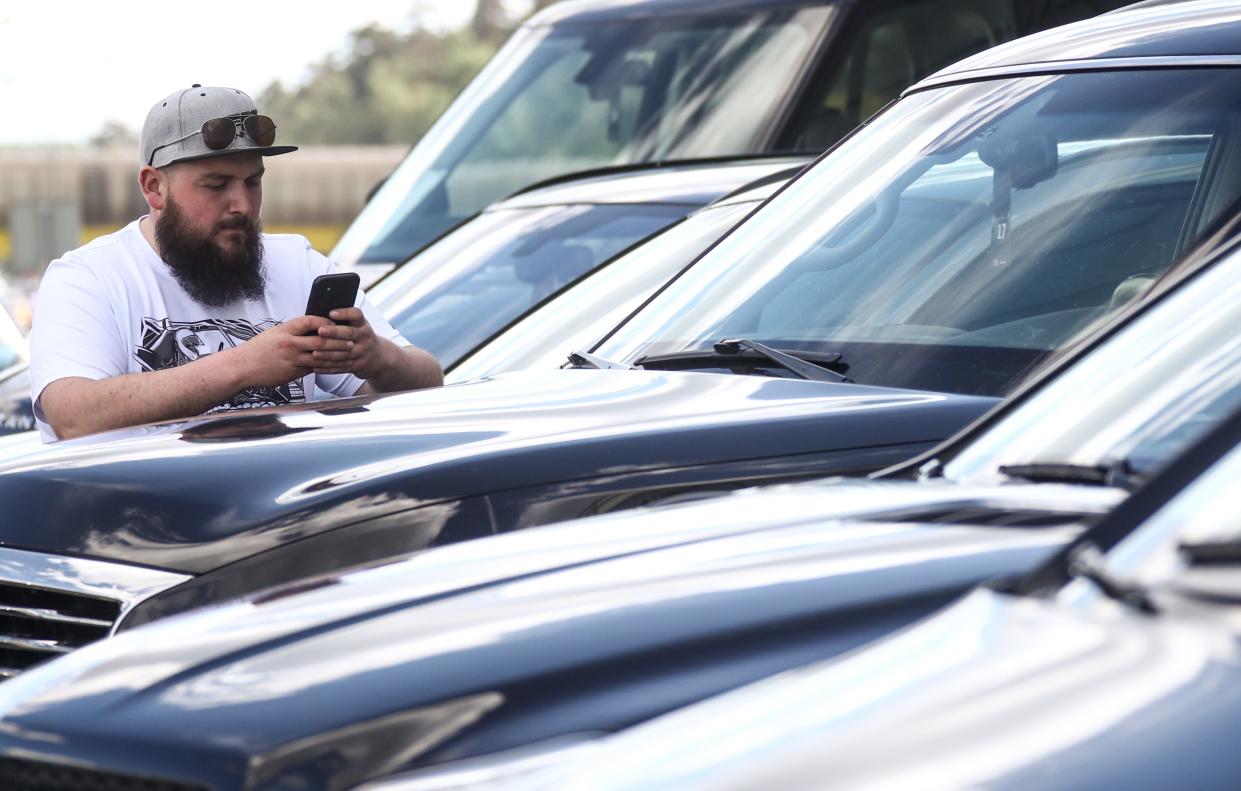 A man looks at his phone on the hood of an SUV at a car dealership