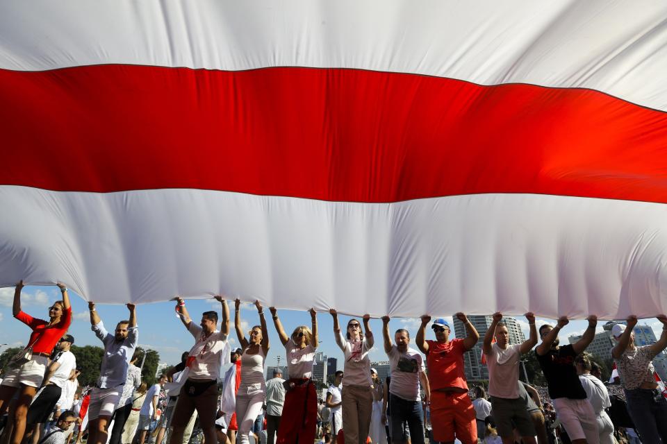 FILE - In this Sunday, Aug. 16, 2020 file photo opposition supporters wave a huge old Belarusian national flag as they rally in the center of Minsk, Belarus. European Union leaders are putting on a show of support Wednesday Aug. 19, 2020 for people protesting in Belarus. Emergency talks will aim to highlight their concern about the contested presidential election and ratchet up pressure on officials linked to the security crackdown that followed. The EU believes that the results of the Aug. 9 polls, which handed President Alexander Lukashenko his sixth term with 80% of the vote, "have been falsified," and the 27-nation bloc is preparing a list of Belarus officials who could be blacklisted from Europe over their roles. (AP Photo/Sergei Grits, File)