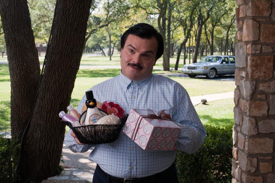 A stout man poses with various gifts for a female friend