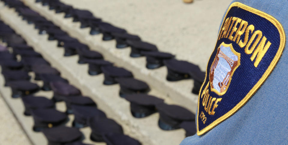 Four lines of dozens of police hats laid out on some steps, behind the badge of an active Paterson Police Department officer.