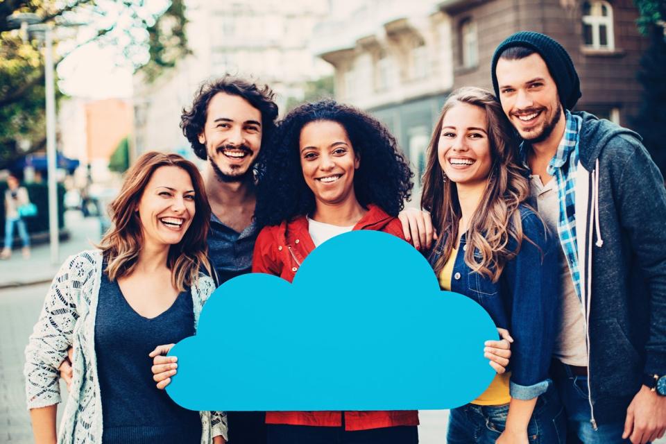 A group of smiling people in the street holding up a large cloud computing logo.