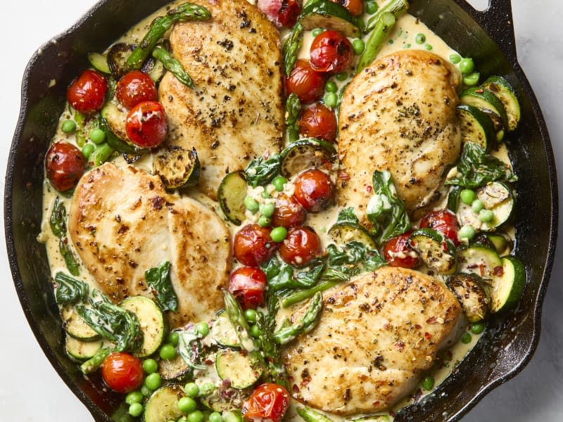 A cast iron skillet filled with chicken primavera showing nicely browned chicken breasts and cooked vegetables in a creamy sauce.