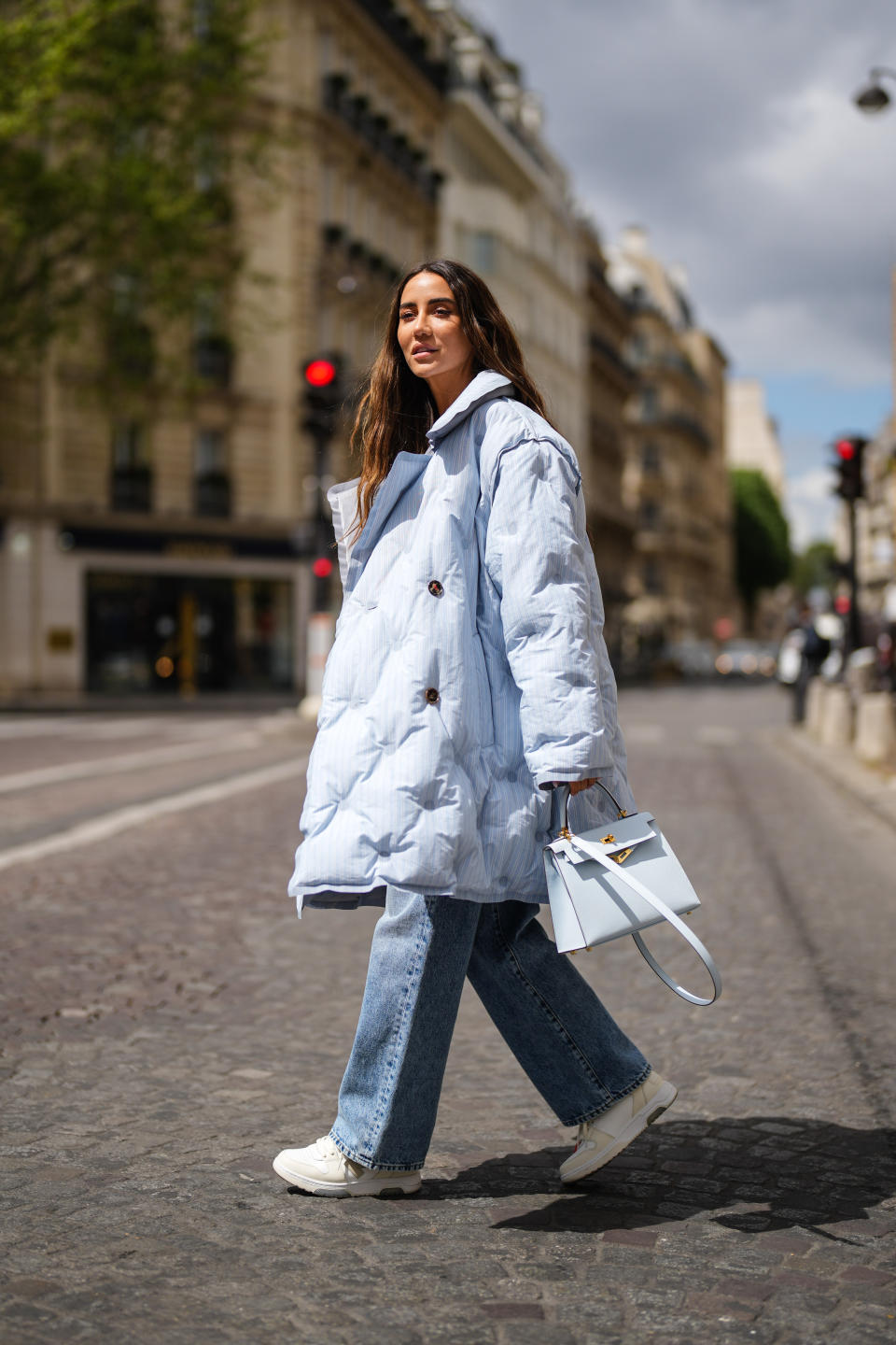 PARIS, FRANCE - MAY 05: Tamara Kalinic wears a pale blue long quilted winter coat from Margiela, blue denim wide-leg jeans pants from Margiela, sneakers shoes with zip-tie from Off-White, a pale blue Hermes Kelly bag, on May 05, 2021 in Paris, France. (Photo by Edward Berthelot/Getty Images)