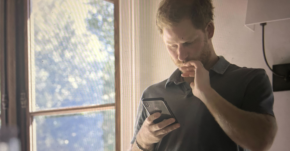 Prince Harry bites his fingernails while reading his phone. 