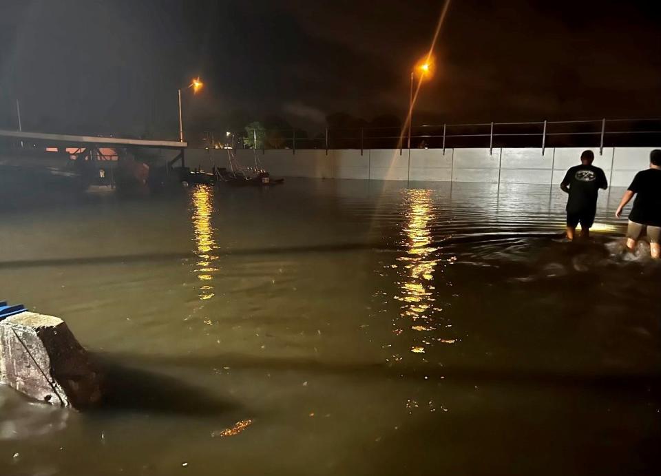 Advanced Roof Technology workers wade through floodwater Saturday night in the company lot. Brightline's concrete retaining wall is in the background.