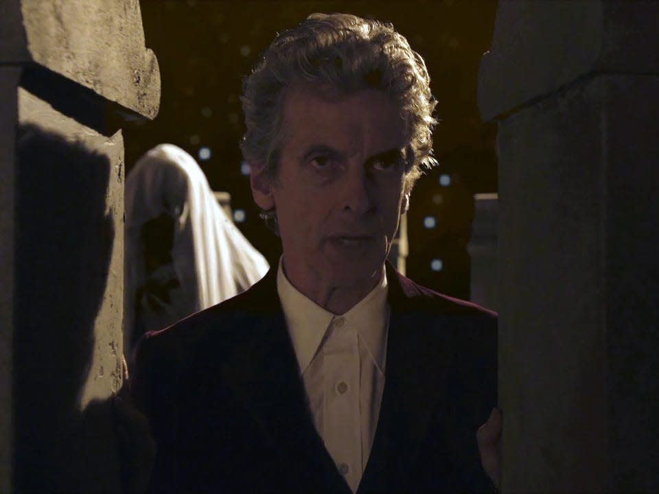 Peter Capaldi in a suit followed by a veiled figure