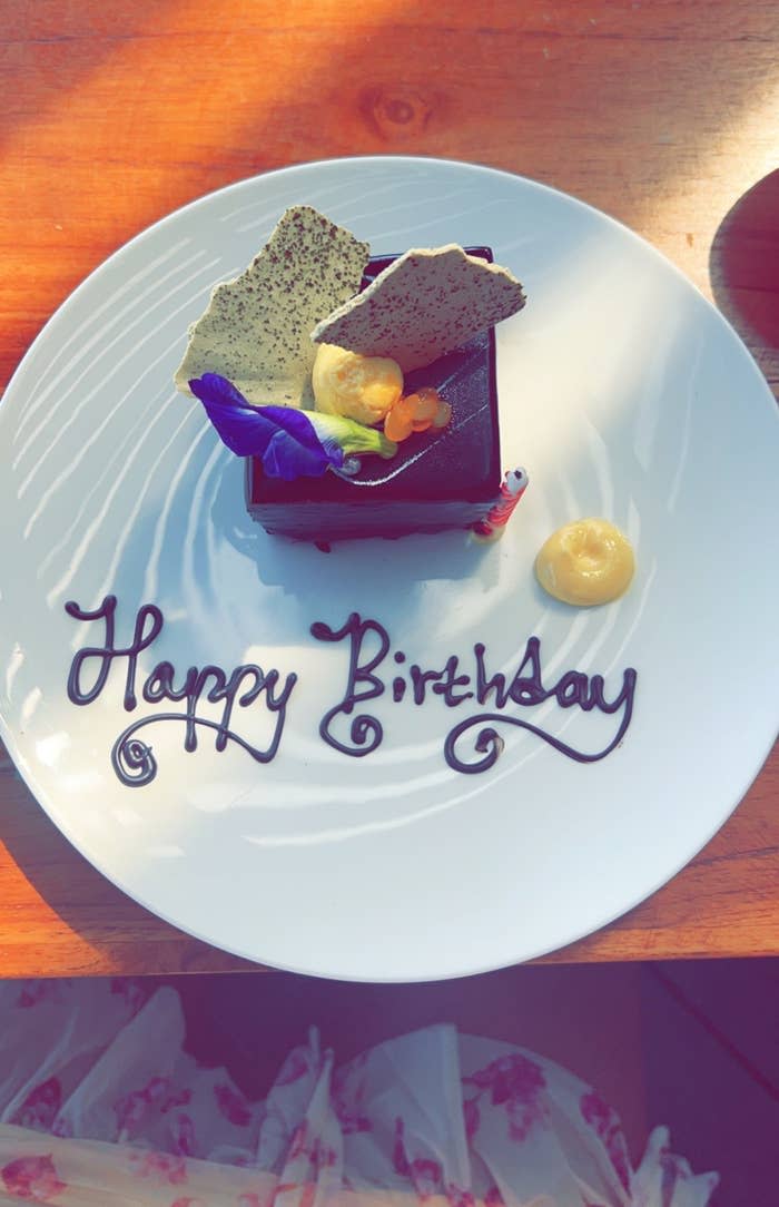 a small square of chocolate cake on a white plate that says "Happy Birthday"