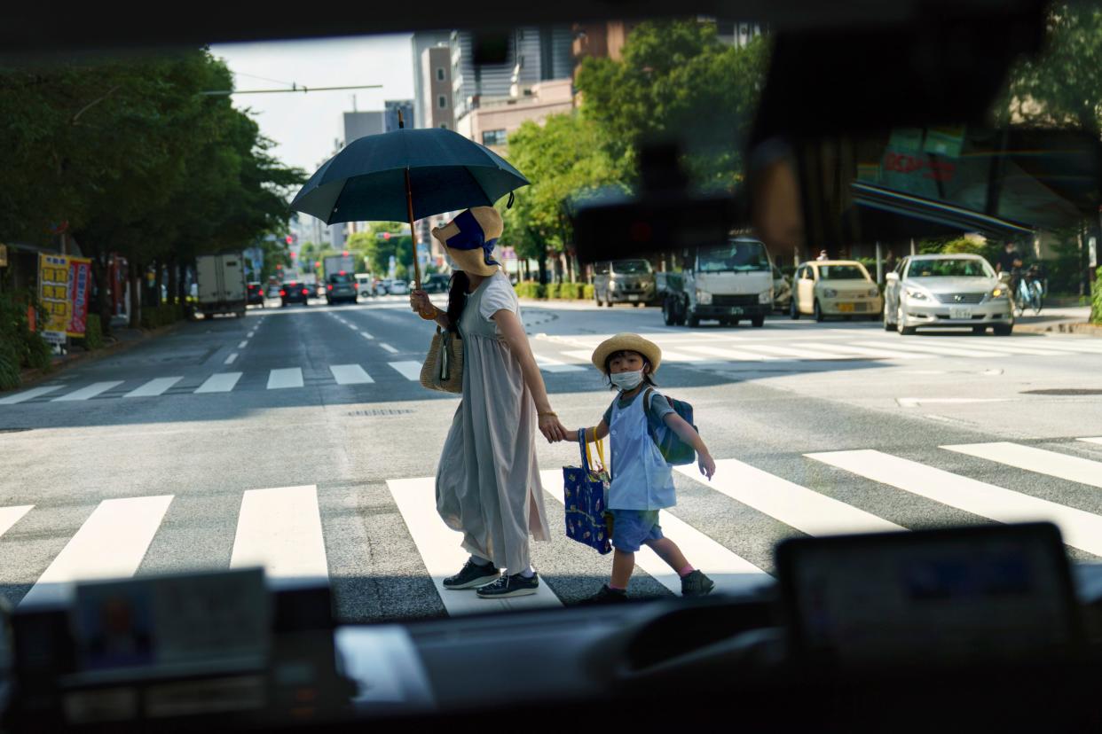 A pedestrian crossing a street with a child is seen through a taxi window in Tokyo, Monday, July 19, 2021. The number of babies born in Japan last year fell for an eighth straight year to a new low, government data showed Tuesday, Feb. 27, 2024, and a top official said it was critical for the country to reverse the trend in the coming half-dozen years.