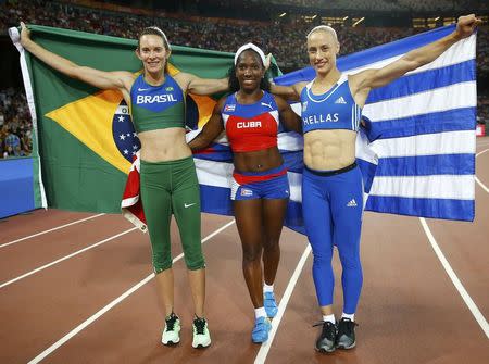 Winner Yarisley Silva of Cuba (C), second placed Fabiana Murer of Brazil (L) and Nikoleta Kyriakopoulou of Greece celebrate with their national flags after competing at the women's pole vault final during the 15th IAAF World Championships at the National Stadium in Beijing, China, August 26, 2015. REUTERS/Kai Pfaffenbach