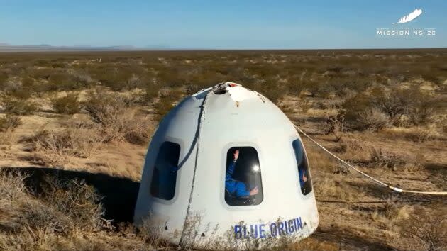 A crew member waves out the window after landing. (Blue Origin via YouTube)