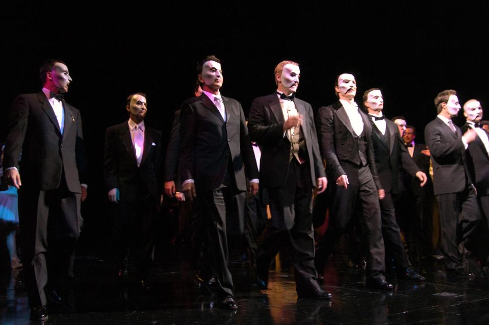 Actors dressed up as "The Phantom of the Opera" walk onstage in masks