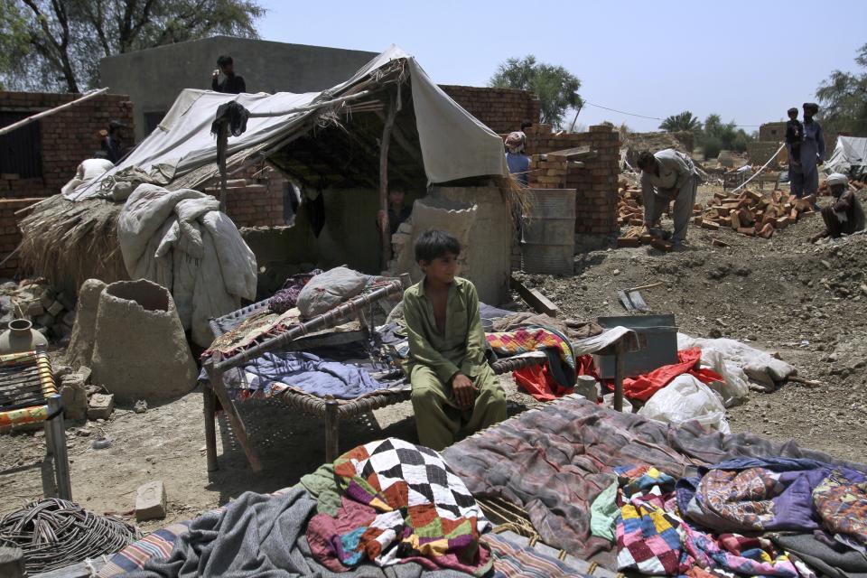 A boy sits outside his tent as laborers reconstruct a house that was damaged in last year's floods, at a village of Rojhan in Rajanpur, a district of Pakistan's Punjab province, Sunday, May 21, 2023. Millions of acres of crops nationwide were destroyed by the waters last year, and a major international aid agency warned that the loss could be felt for years. (AP Photo/Asim Tanveer)