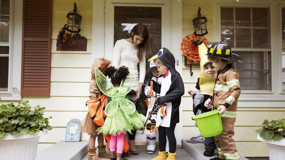 woman distributing candies to children in halloween costumes during trick or treating