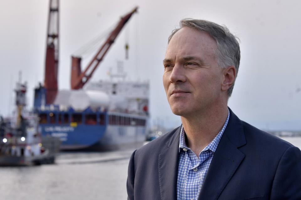 Mayor Jon Mitchell poses for a photo in front of the UHL Felicity ship that carried massive parts for offshore wind turbines docked in New Bedford Harbor, Wednesday, May 24, 2023, in New Bedford, Mass. Once assembled by developer Vineyard Wind, the turbines at sea will stand more than 850 feet high. (AP Photo/Josh Reynolds)