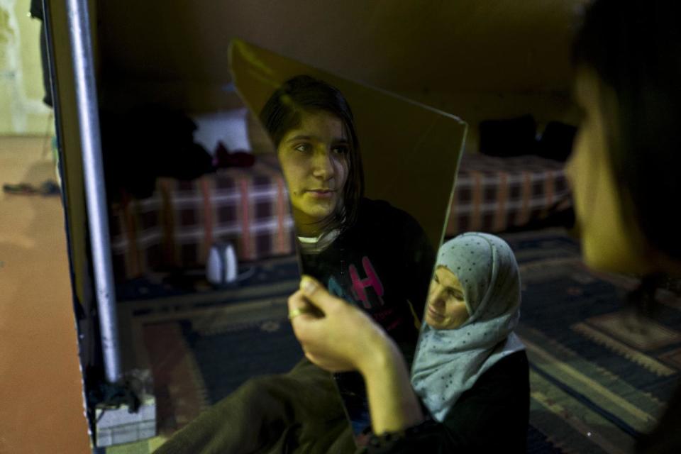 In this Tuesday, Jan. 17, 2017 photo, Syrian refugee Kulnawaz Youssef, 13, looks at herself in a mirror at her tent in Kalochori refugee camp on the outskirts of the northern Greek city of Thessaloniki. Many migrants living in this warehouse tent camp and another one nearby are feeling burned out. They try to keep busy as they dream of a better life in Western Europe and not let boredom or depression set in. (AP Photo/Muhammed Muheisen)