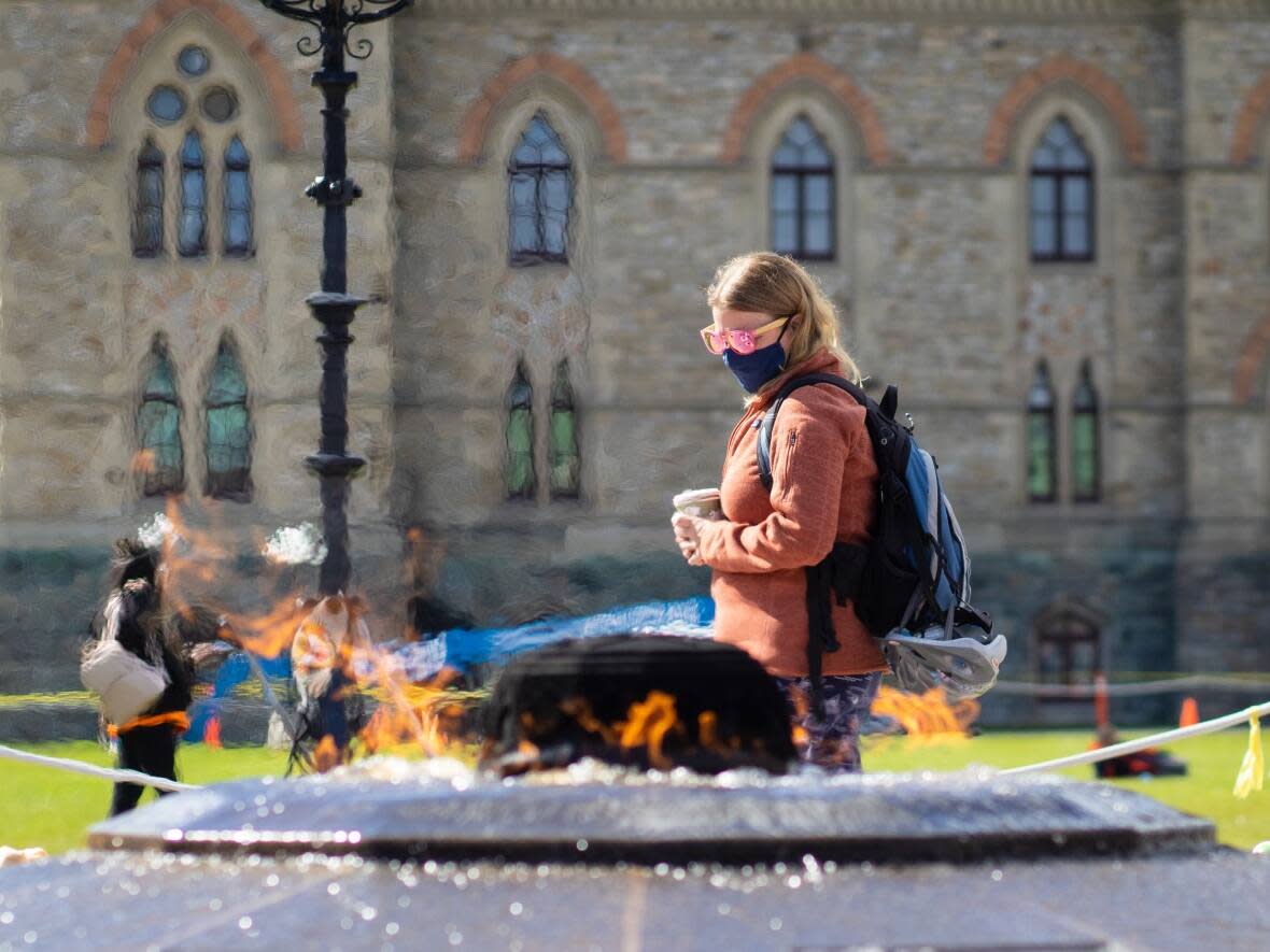 A person in sunglasses and a mask walks past the Centennial Flame in Ottawa on Sept. 30, 2021, during the COVID-19 pandemic. (Trevor Pritchard/CBC - image credit)