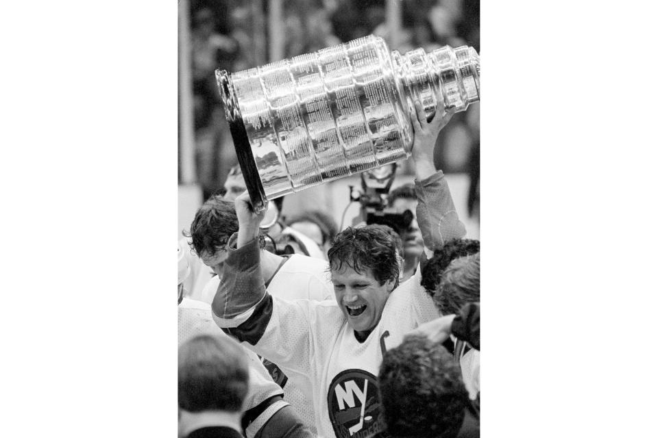 FILE - New York Islanders captain Dennis Potvin raises the Stanley Cup, after his team beat the Edmonton Oilers 4-2 at the Nassau Coliseum, in Uniondale, N.Y., May 17, 1983. As Georgia begins its quest for an unprecedented three-peat in college football, those who have been there before can provide some helpful perspective on what it takes to keep winning titles year after year after year. Potvin was captain of the New York Islanders when they captured four straight Stanley Cup titles in the early ‘80s.(AP Photo/Richard Drew, File)