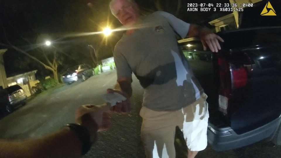 In this image from video provided by the Tampa Police Department, Joseph Ruddy, a prosecutor with the U.S. Attorney’s Office in Tampa, hands his business card to Officer Taylor Grant, outside his home in Temple Terrace, Fla., on the evening of July 4, 2023. When police arrived at his house to investigate a hit-and-run, Ruddy, one of the nation’s most prolific federal narcotics prosecutors, was so drunk he could barely stand up straight, leaning on the tailgate of his pickup to keep his balance. (Officer Taylor Grant/Tampa Police Department)