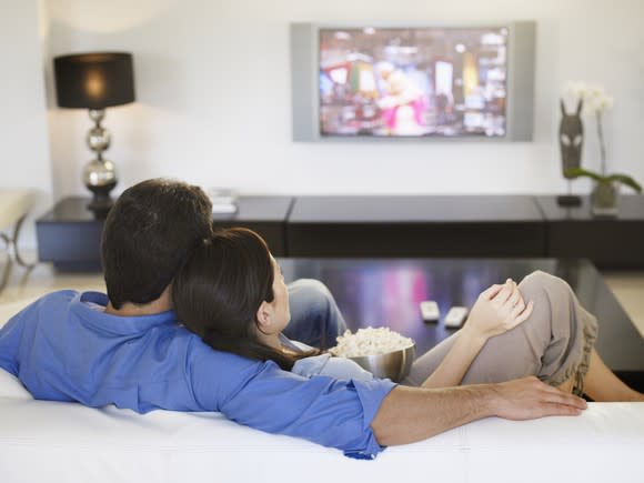 A man and woman sitting on a couch watching television.