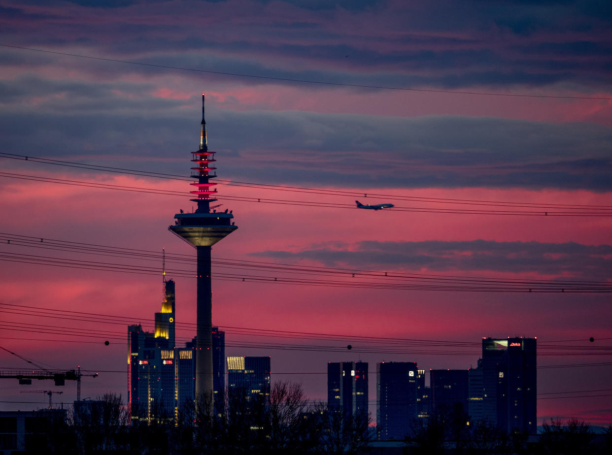 An aircraft passes a television tower and buildings of the banking district as it approaches the airport in Frankfurt, Germany, just before sunrise on Sunday, Feb. 16, 2020. (AP Photo/Michael Probst)