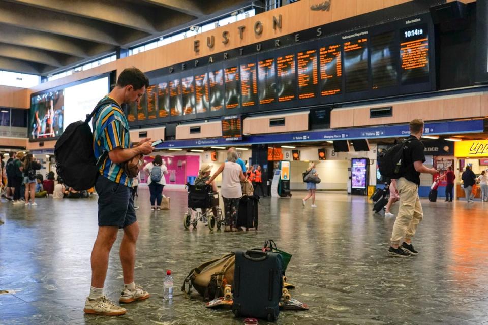 Passengers await their trains to be announced, at a quiet Euston station, in Londo (AP)