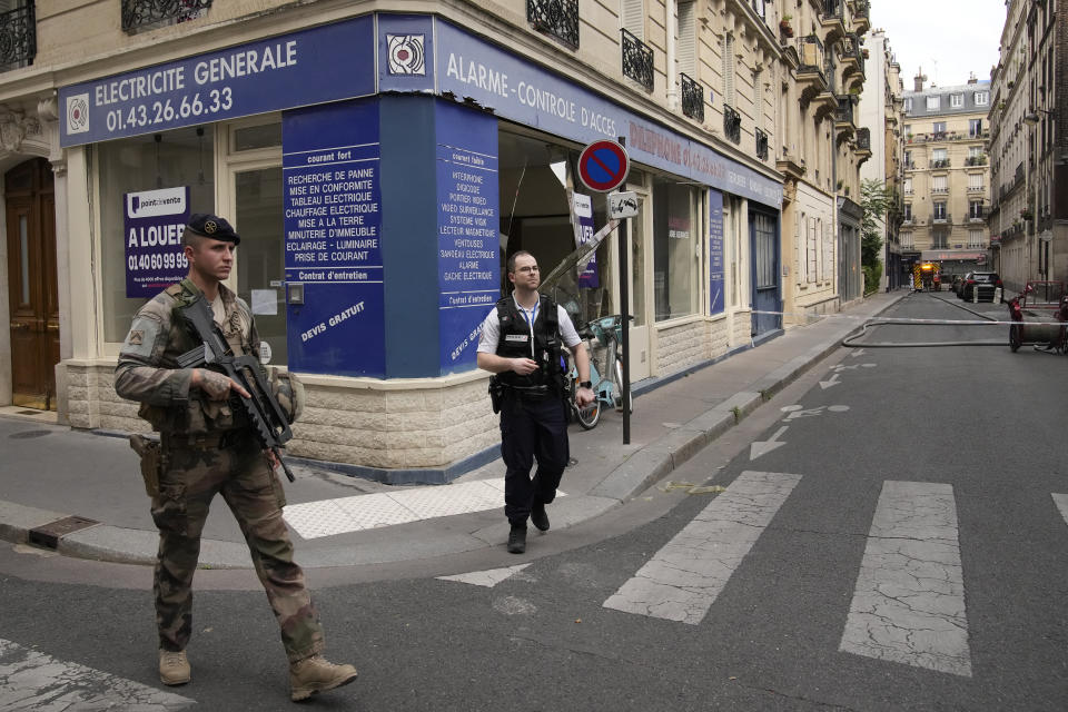 A soldier an a police officer secure the streets as firemen fight a blaze Wednesday, June 21, 2023 in Paris. Firefighters fought a blaze on Paris' Left Bank that is sent smoke soaring over the domed Pantheon monument and prompted evacuation of buildings in the neighborhood, police said. Local media cited witnesses describing a large explosion preceding the fire, and saying that part of a building collapsed. (AP Photo/Christophe Ena)