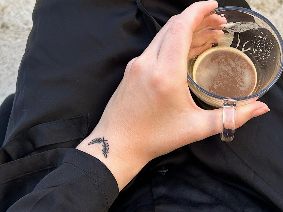 The author holding a cup of coffee. A tattoo of an olive branch can be seen on her wrist.