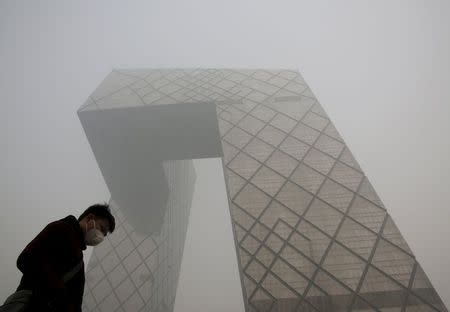 A man wearing a mask walks past the China Central Television (CCTV) building during a heavily polluted day in Beijing, November 30, 2015. REUTERS/Kim Kyung-Hoon