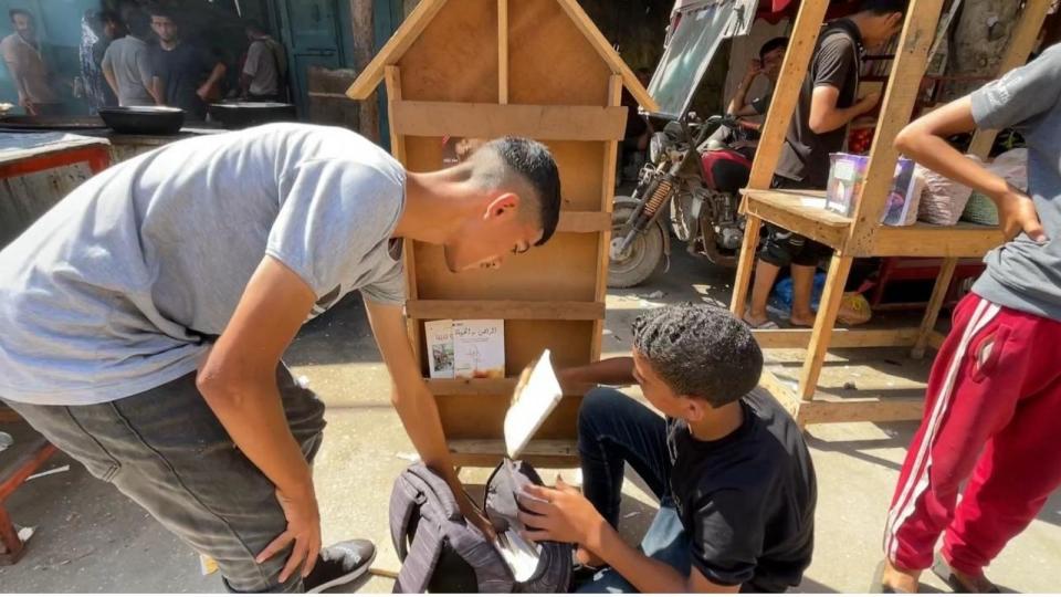 PHOTO: Abdul Hakim, Marwa’s cousin, with Marwa’s little brother’s help, arranges their bookstore in order to attract the eyes of passers-by on the streets of Deir Al-Balah. (Diaa Ostaz/ABC News)