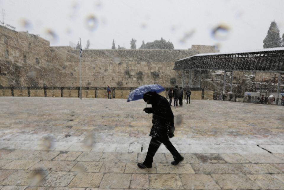 A man holding an umbrella walks as snow falls at the Western Wall in Jerusalem's Old City December 12, 2013. Snow fell in Jerusalem and parts of the occupied West Bank where schools and offices were widely closed and public transport was paused. REUTERS/Ammar Awad (JERUSALEM - Tags: RELIGION ENVIRONMENT)