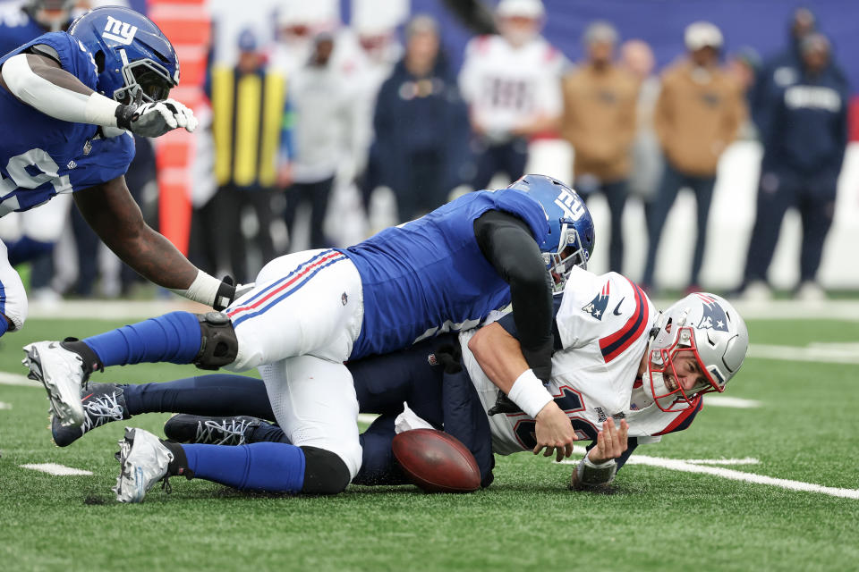 EAST RUTHERFORD, NEW JERSEY - NOVEMBER 26: Mac Jones #10 of the New England Patriots fumbles the ball while being tackled by Kayvon Thibodeaux #5 of the New York Giants during the second quarter at MetLife Stadium on November 26, 2023 in East Rutherford, New Jersey. (Photo by Al Bello/Getty Images)