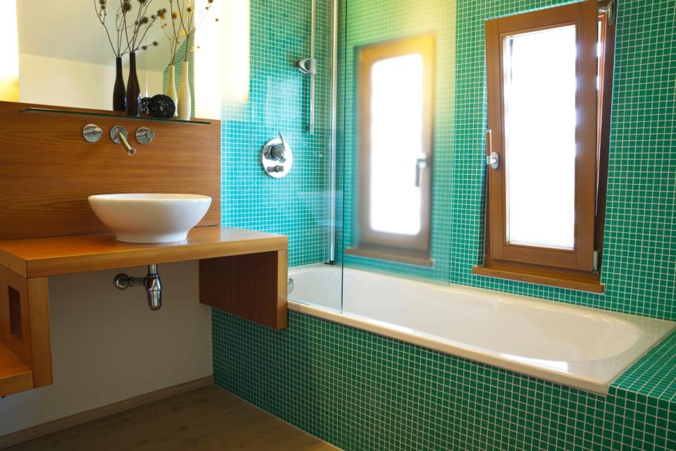 green-tiled-bathtub-next-to-a-wood-counter-with-a-white-basin-sink