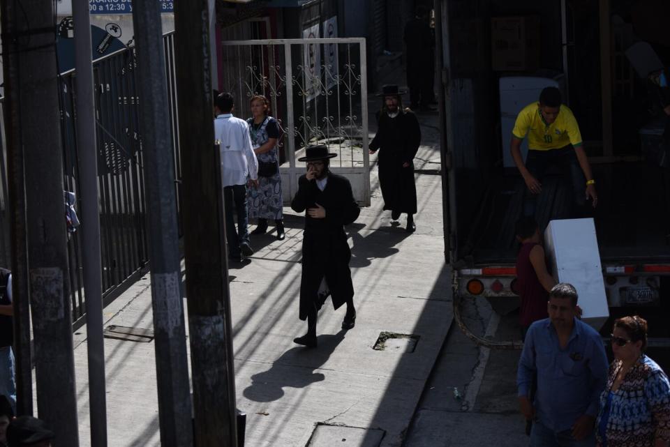 Two people in dark hats and clothing stand near a gate and a truck where people are moving their belongings