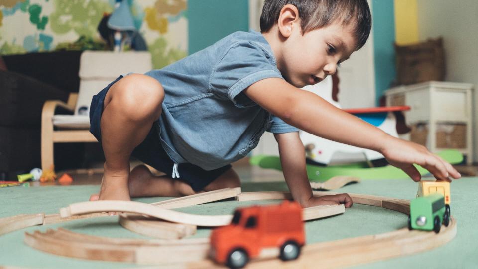 Cute little boy playing with wooden train on the floor at home.