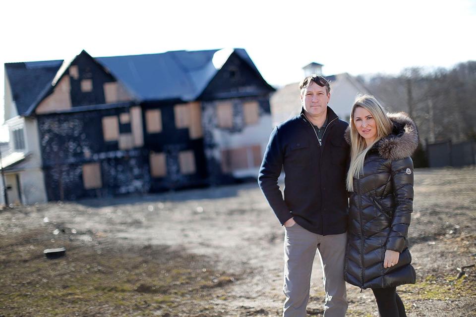 Pat and Haley Cutter stand on the lot their home once occupied, with a damaged neighboring home in the background.