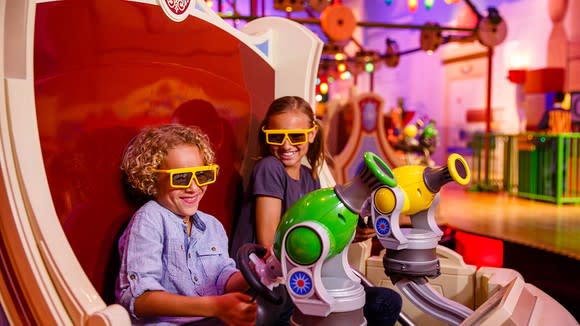 Two young riders on Toy Story's Midway Mania attraction wearing yellow 3D glasses.