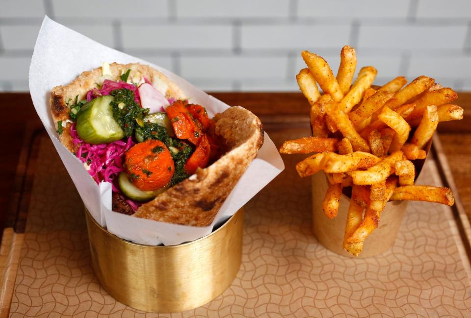 A sandwich filled with hummus, greens, brisket, pickled cabbage, cucumbers, radishes and spicy carrots with a side of Brassica fries sprinkled with paprika and sumac at Brassica.