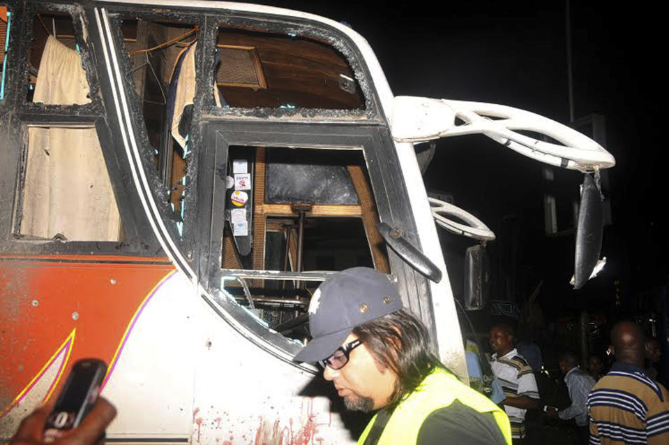 People stand near to a bus with windows shattered after an explosion, in Mombasa Kenya, Saturday, May, 3, 2014. At least three have been confirmed dead and several others injured in twin explosions in the coastal city of Mombasa, Kenya, police said on Saturday. Mombasa Country police commander, Robert Kitur said they have not established the cause of the explosions at Reef Hotel Nyali and Mwembe Tayari in town. (AP Photo)