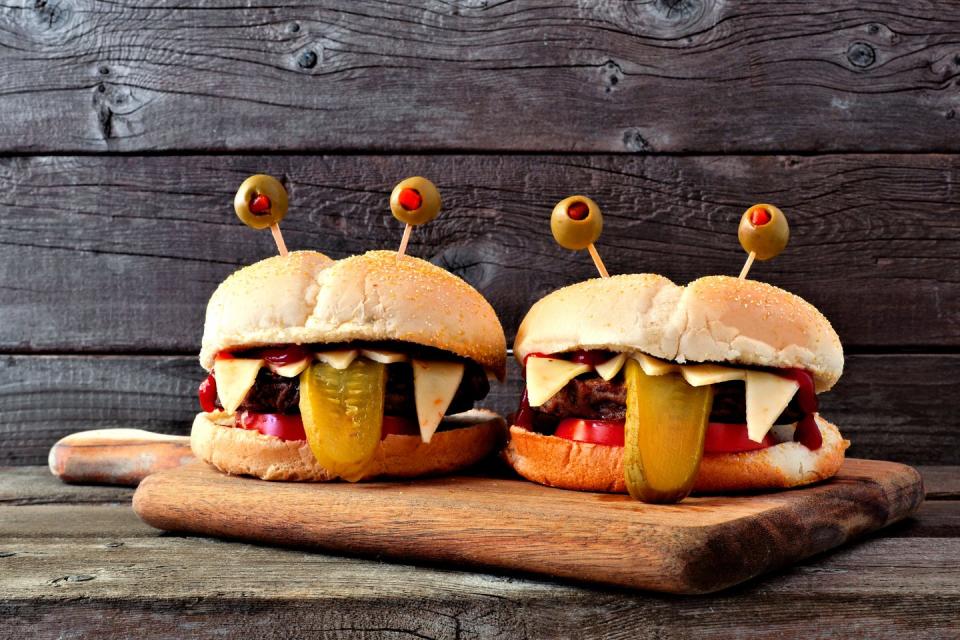 <p>Make your burgers as you normally would and just get festive with the toppings. Cut the cheese to look like teeth and top with some toothpick <del>eyes</del> — we mean olives. </p>