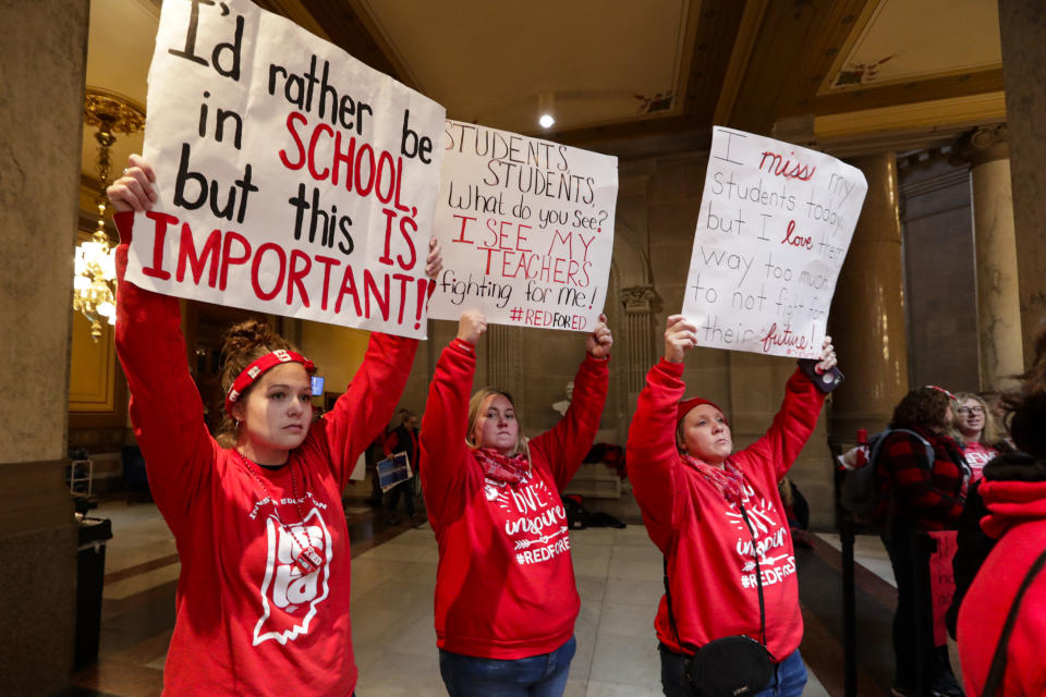 Indiana teachers wearing red have carry signs as they hold rally at the Statehouse in Indianapolis, Tuesday, Nov. 19, 2019, calling for further increasing teacher pay in the biggest such protest in the state amid a wave of educator activism across the country. Teacher unions says about half of Indiana's nearly 300 school districts are closed while their teachers attend Tuesday's rally while legislators gather for 2020 session organization meetings.(AP Photo/Michael Conroy)