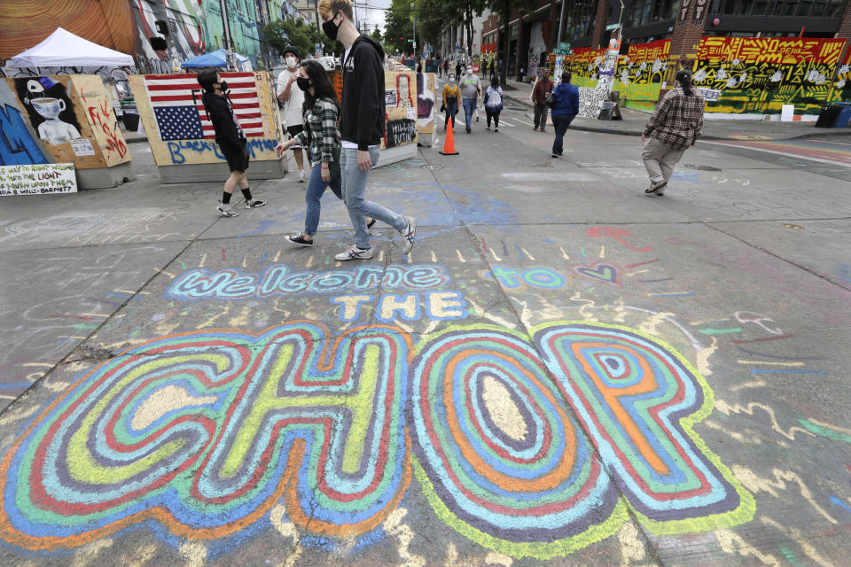 Pedestrians walk Sunday, June 21, 2020, in Seattle, where streets are blocked off in what has been named the Capitol Hill Occupied Protest (CHOP) zone. Police pulled back from several blocks of the city's Capitol Hill neighborhood near the Police Department's East Precinct building earlier in the month after clashes with people protesting the death of George Floyd. (AP Photo/Elaine Thompson)