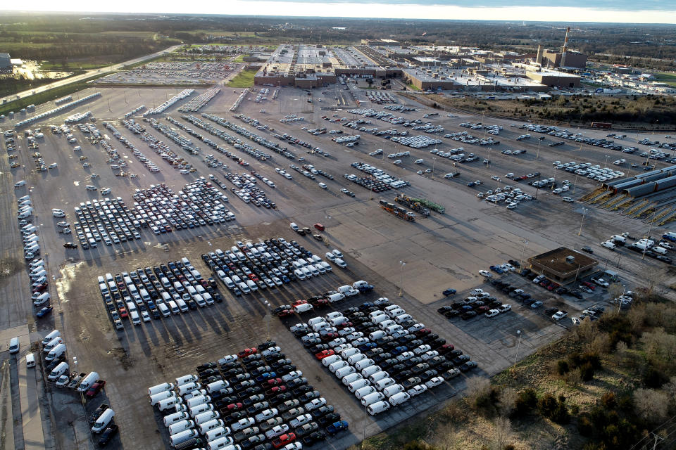 In this aerial photo, a General Motors assembly plant is seen at top right while mid-sized pickup trucks and full-size vans currently produced at the plant are seen in a parking lot outside Wednesday, March 24, 2021, in Wentzville, Mo. As the U.S. economy awakens from its pandemic-induced slumber, a vital cog is in short supply: the computer chips that power our cars and other vehicles, and a vast number of other items we take for granted. Ford, GM and Stellantis have started building vehicles without some computers, putting them in storage with plans to retrofit them later. (AP Photo/Jeff Roberson)