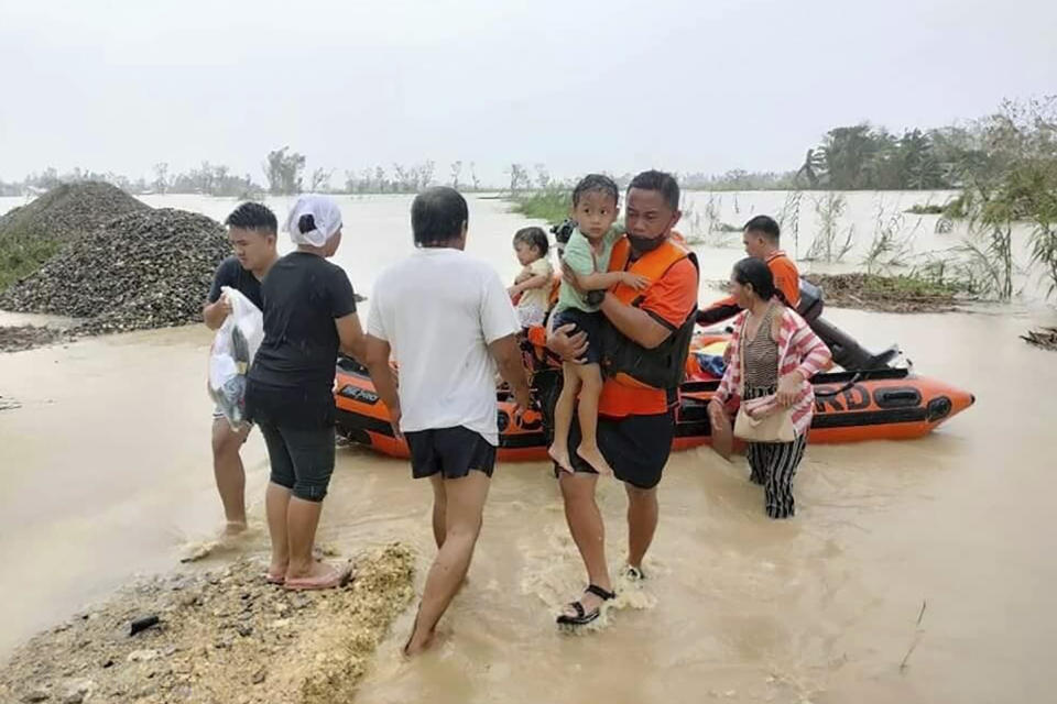 CORRECTS THE AREA TO NEGROS OCCIDENTAL, INSTEAD OF LOBOC, BOHOL - In this photo provided by the Philippine Coast Guard, rescuers carry a child as they assist residents who were trapped in their homes after floodwaters caused by Typhoon Rai inundated their village in Negros Occidental, central Philippines on Friday, Dec. 17, 2021. The strong typhoon engulfed villages in floods that trapped residents on roofs, toppled trees and knocked out power in southern and central island provinces, where more than 300,000 villagers had fled to safety before the onslaught, officials said. (Philippine Coast Guard via AP)