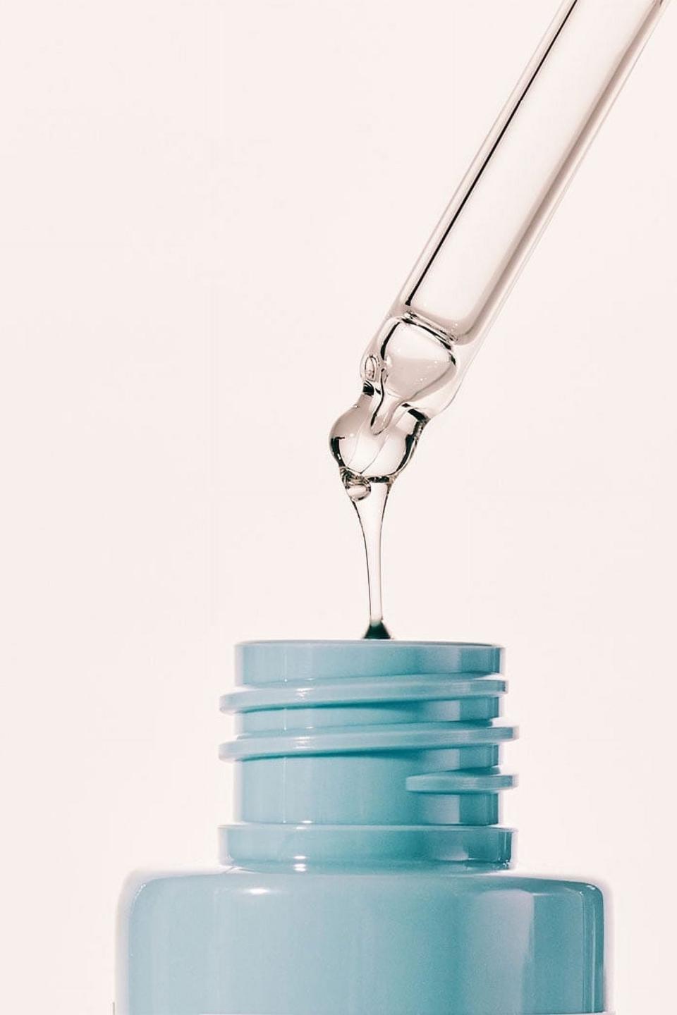 Dropper dispensing clear serum into a blue bottle