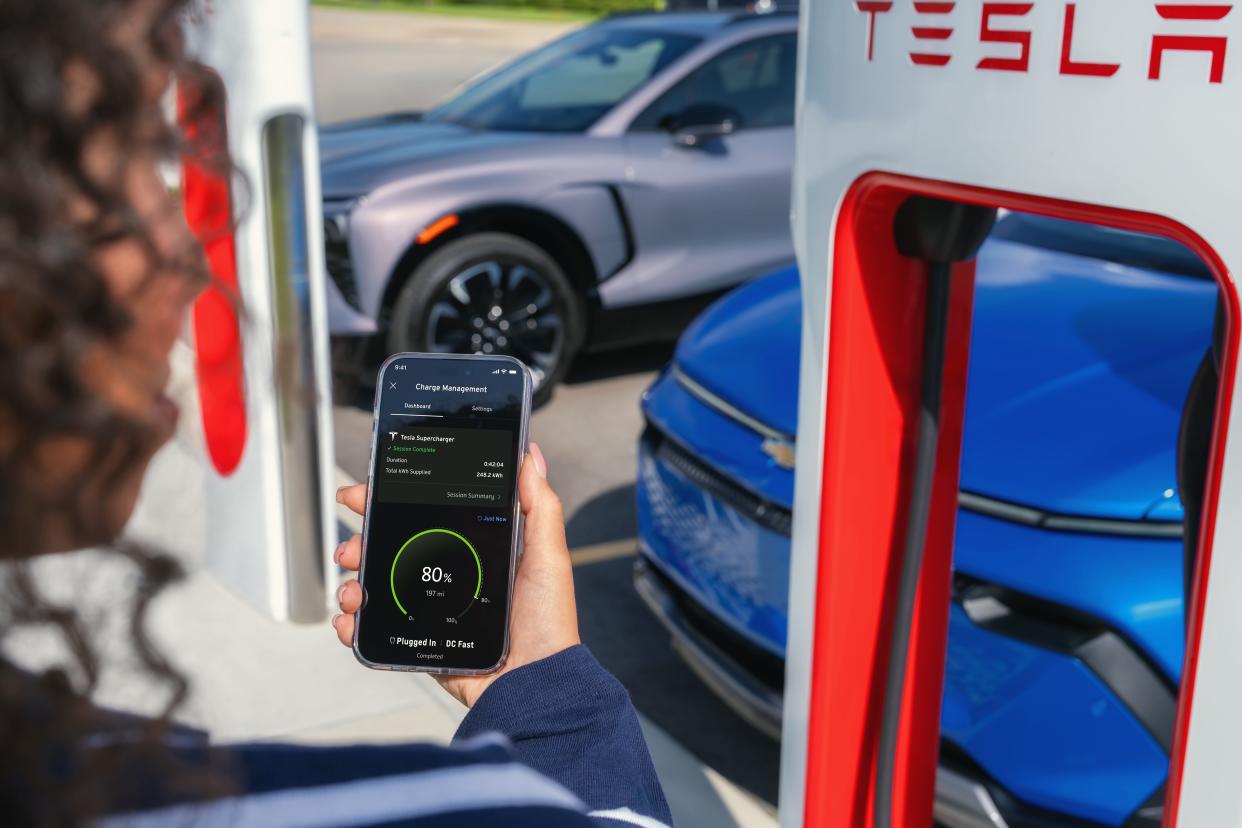 A person uses a smartphone app to charge their Chevrolet electric vehicle at a Tesla-branded Supercharger.